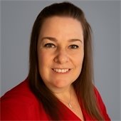 woman with brown hair in a red shirt standing in front of a gray background